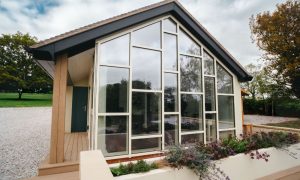 Contemporary timber and glass pavilion house with floor-to-ceiling windows, minimalist architecture set in landscaped countryside garden
