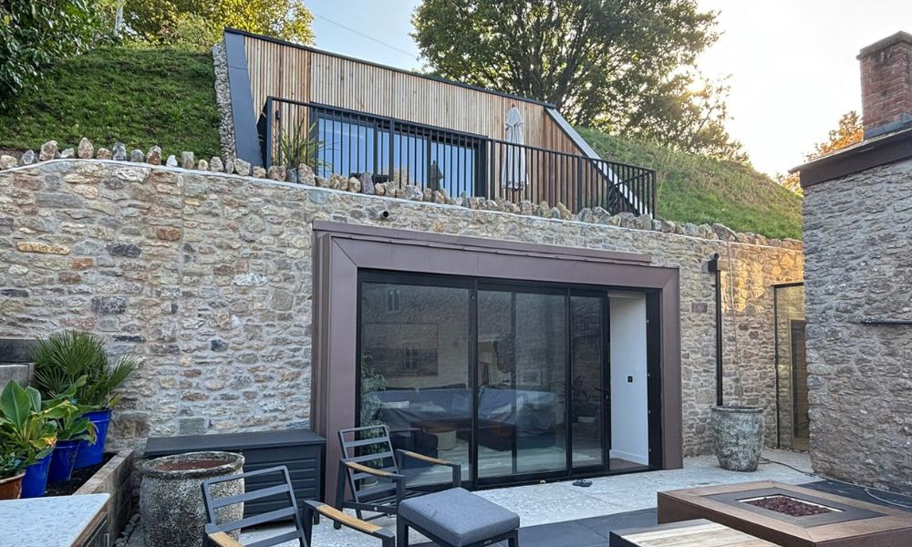 Contemporary stone house with underground bedroom suite, floor-to-ceiling glass doors, and landscaped terrace featured in Architecture Vogue magazine