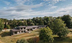 Contemporary timber-clad countryside home with standing seam metal roof, set within landscaped gardens and mature trees – modern sustainable architecture featured in Architecture Vogue.