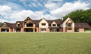 Luxury modern Tudor-style country house with exposed timber framing, red brick façade, large glass windows and landscaped lawn, featured in Architecture Vogue magazine.