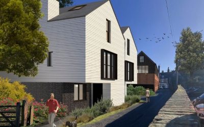Contemporary gabled house with white cladding and dark brick base along a narrow village lane, modern residential architecture surrounded by trees and landscaped gardens
