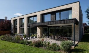 Modern two-story brick house with floor-to-ceiling glass windows, minimalist architecture, and landscaped garden terrace featured in Architecture Vogue magazine