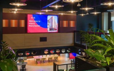 Modern co-working space interior in Manchester featuring contemporary lighting, indoor greenery, and open-plan seating with digital display screens