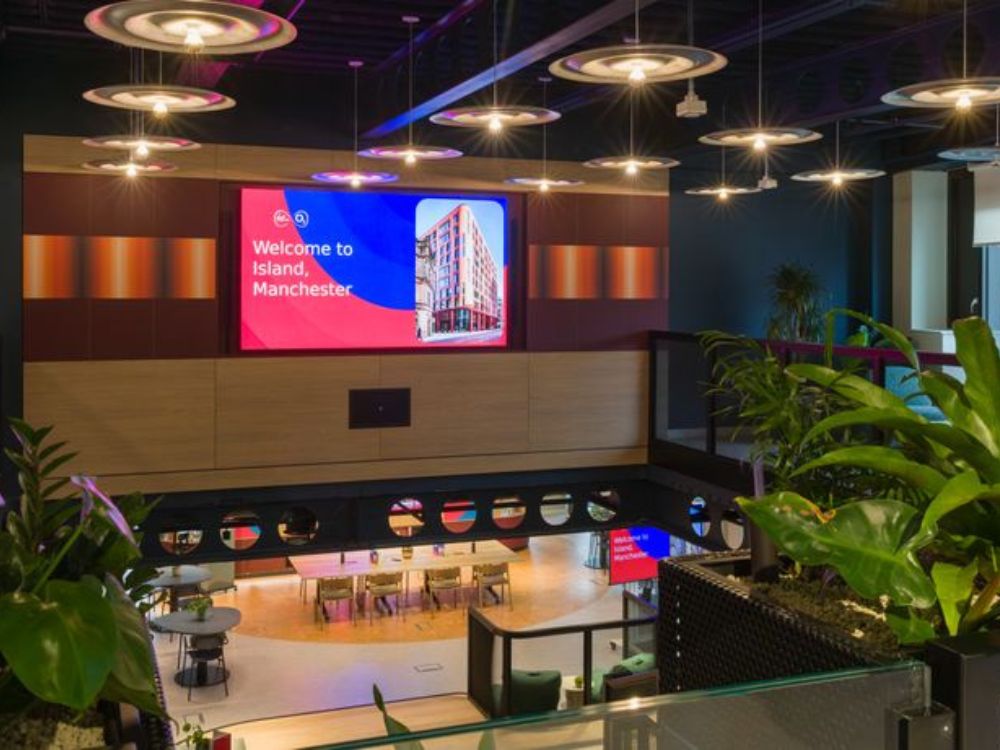 6 Modern co-working space interior in Manchester featuring contemporary lighting, indoor greenery, and open-plan seating with digital display screens