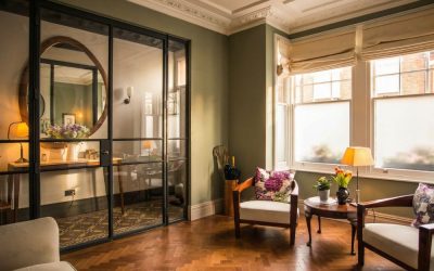 “Warm living room with herringbone wood floor, glass partition and natural light, featured in Architecture Magazine