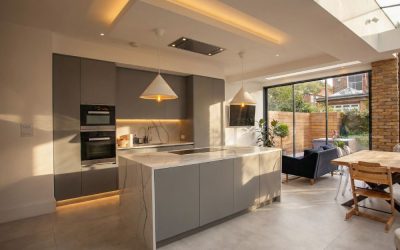 Sunlit contemporary open-plan kitchen extension with marble waterfall island, skylight ceiling, bespoke grey cabinetry, pendant lighting, and seamless indoor-outdoor living — featured in Architecture Vogue magazine