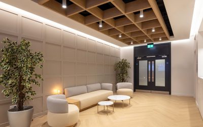 Modern minimalist lounge interior with geometric wooden coffered ceiling, soft neutral seating, and warm ambient lighting in a contemporary office space